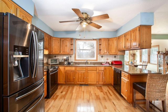 kitchen featuring sink, appliances with stainless steel finishes, a kitchen bar, kitchen peninsula, and light wood-type flooring