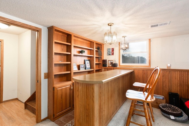 office space with wood walls, a chandelier, a textured ceiling, light wood-type flooring, and indoor bar