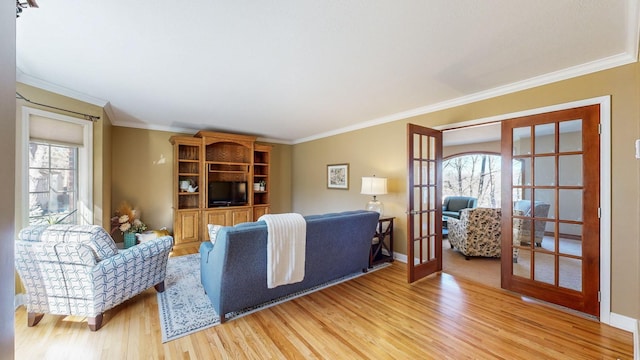 living room with light hardwood / wood-style flooring, crown molding, a wealth of natural light, and french doors