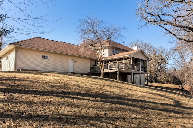 rear view of property featuring a wooden deck, a yard, and a sunroom