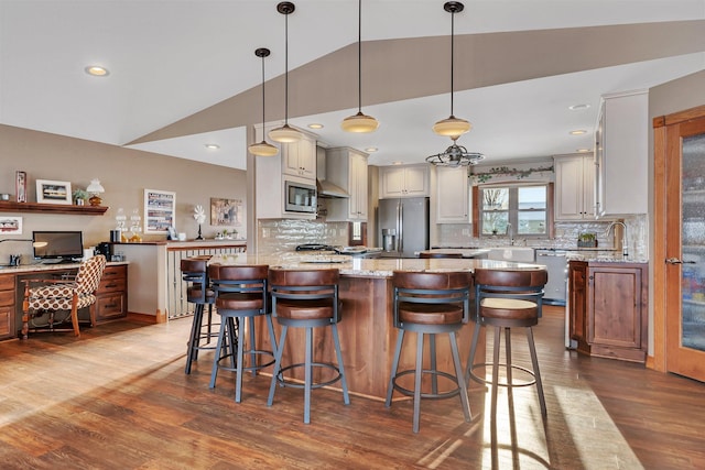 kitchen with decorative light fixtures, lofted ceiling, a breakfast bar area, light stone counters, and stainless steel appliances