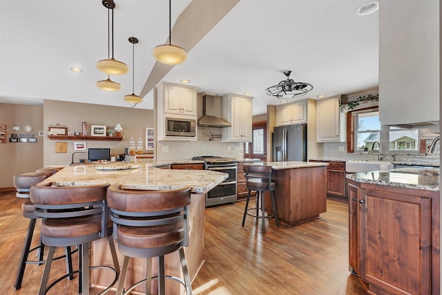 kitchen featuring a spacious island, a breakfast bar, appliances with stainless steel finishes, light stone countertops, and wall chimney range hood