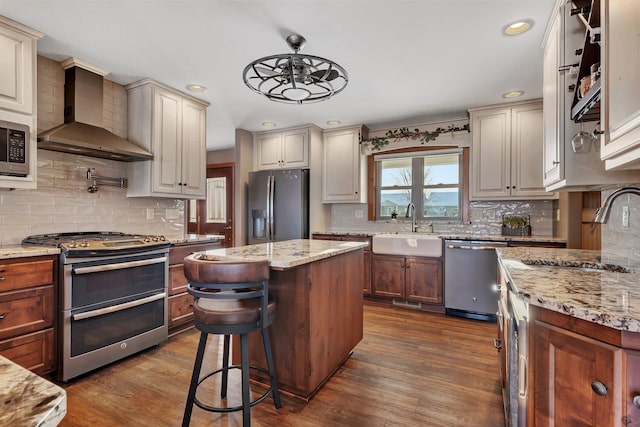 kitchen featuring wall chimney range hood, sink, stainless steel appliances, a center island, and dark hardwood / wood-style flooring