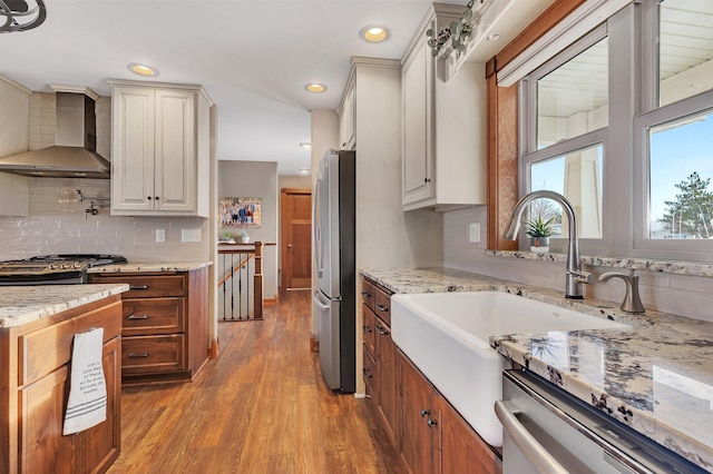 kitchen with appliances with stainless steel finishes, wall chimney exhaust hood, light hardwood / wood-style floors, and backsplash