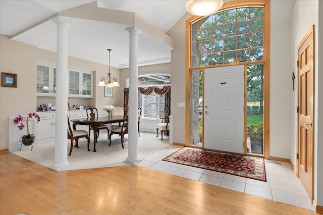 foyer entrance featuring baseboards, light wood finished floors, an inviting chandelier, and ornate columns