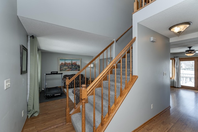 staircase with ceiling fan, a textured ceiling, baseboards, and wood finished floors