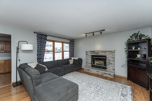 living room with a brick fireplace, baseboards, light wood-style flooring, and a textured ceiling