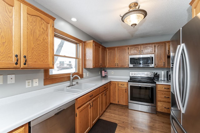 kitchen with stainless steel appliances, wood finished floors, a sink, light countertops, and brown cabinetry