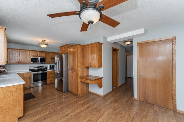 kitchen with baseboards, light countertops, appliances with stainless steel finishes, light wood-type flooring, and brown cabinets