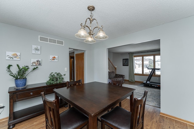 dining room featuring light wood-style floors, a notable chandelier, visible vents, and a textured ceiling