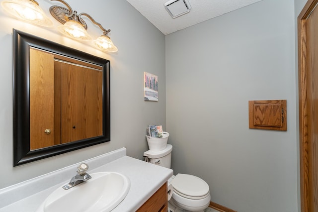 bathroom with a textured ceiling, vanity, and toilet