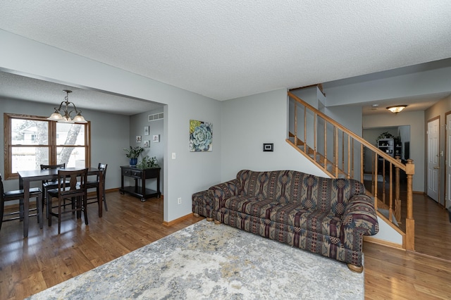 living room featuring a textured ceiling, visible vents, baseboards, stairway, and dark wood-style floors