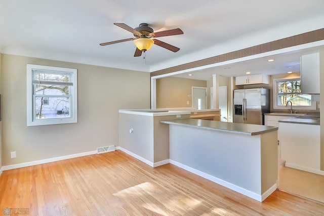 kitchen featuring stainless steel refrigerator with ice dispenser, kitchen peninsula, light wood-type flooring, and white cabinets