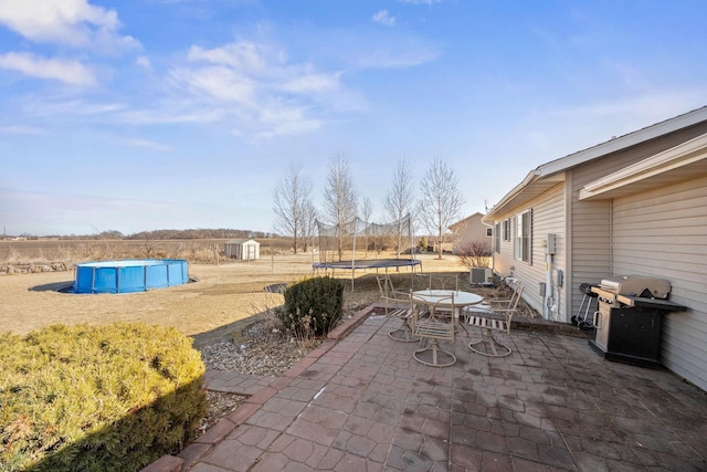 view of patio with central AC, area for grilling, a shed, and a trampoline