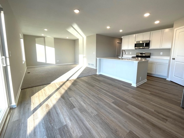 kitchen featuring an island with sink, appliances with stainless steel finishes, white cabinets, and dark hardwood / wood-style flooring