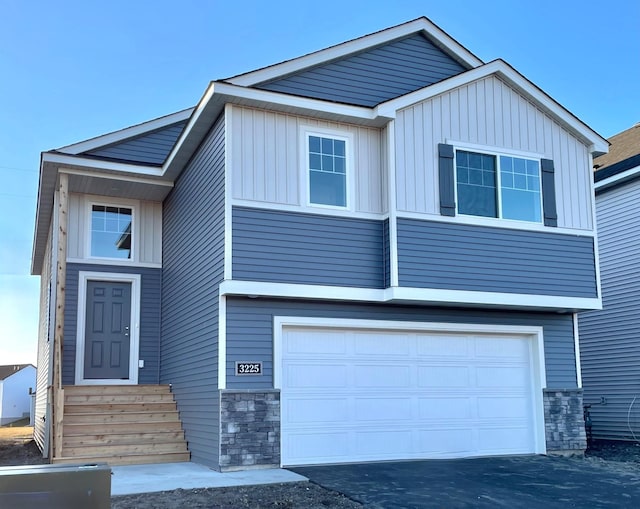 view of front of house with board and batten siding, stone siding, a garage, and aphalt driveway