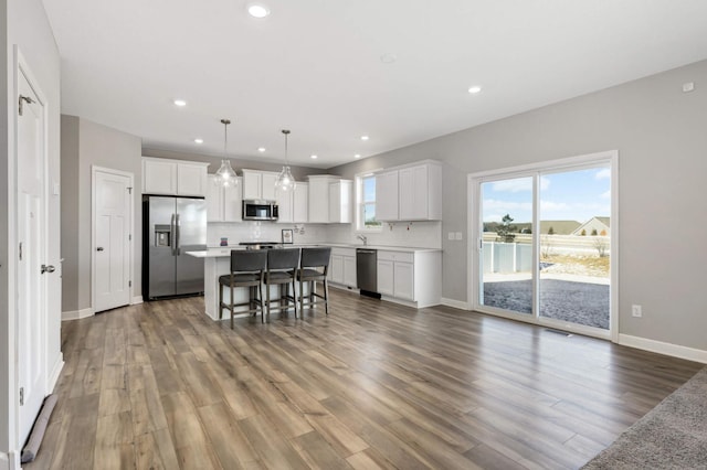 kitchen with a breakfast bar area, white cabinetry, hanging light fixtures, stainless steel appliances, and a center island