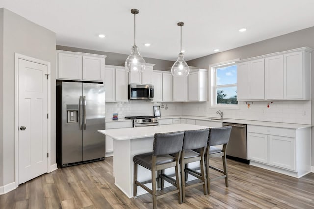 kitchen with appliances with stainless steel finishes, a kitchen island, white cabinetry, hanging light fixtures, and light wood-type flooring