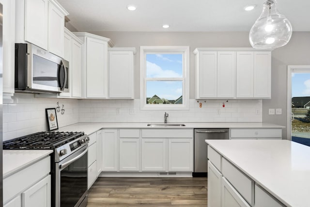 kitchen featuring sink, white cabinets, hardwood / wood-style flooring, hanging light fixtures, and stainless steel appliances