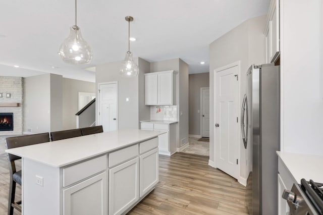 kitchen featuring a breakfast bar area, stainless steel refrigerator, a kitchen island, pendant lighting, and white cabinets