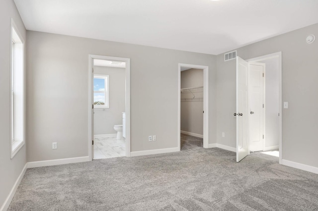 unfurnished bedroom featuring ensuite bathroom, a spacious closet, light carpet, and a closet