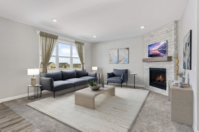 living room featuring a stone fireplace, recessed lighting, wood finished floors, and baseboards