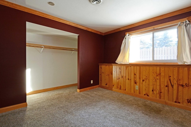 unfurnished bedroom featuring ornamental molding, carpet flooring, wooden walls, and a closet