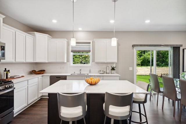 kitchen with appliances with stainless steel finishes, sink, white cabinets, hanging light fixtures, and a center island