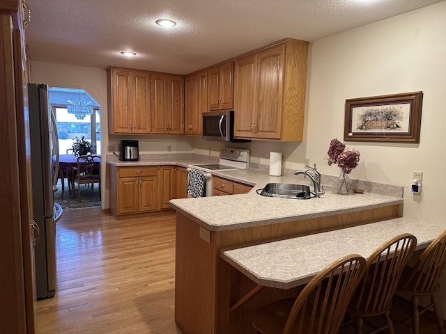 kitchen with sink, appliances with stainless steel finishes, a kitchen breakfast bar, light hardwood / wood-style floors, and kitchen peninsula