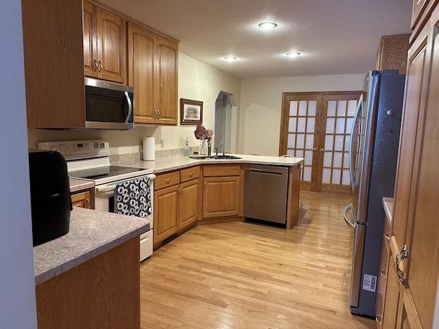 kitchen with sink, a textured ceiling, light wood-type flooring, appliances with stainless steel finishes, and kitchen peninsula