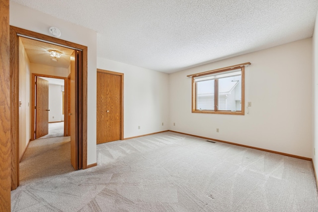 interior space featuring a closet, light colored carpet, visible vents, a textured ceiling, and baseboards