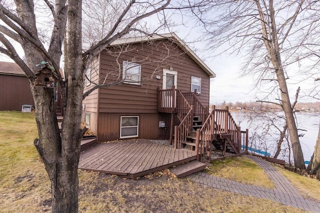 back of property with a deck with water view and a lawn