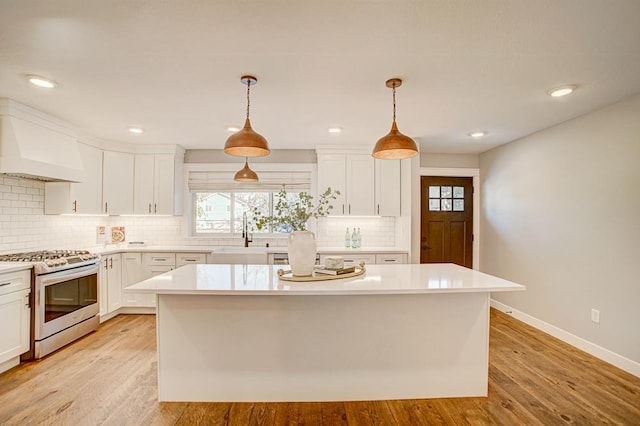 kitchen featuring pendant lighting, sink, premium range hood, stainless steel gas stove, and a kitchen island