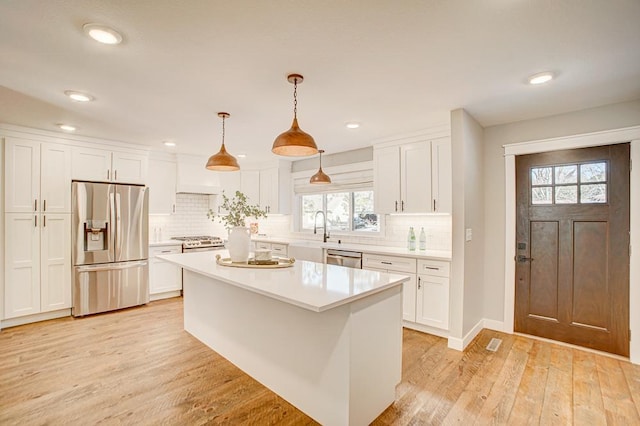 kitchen with white cabinetry, hanging light fixtures, a kitchen island, and appliances with stainless steel finishes