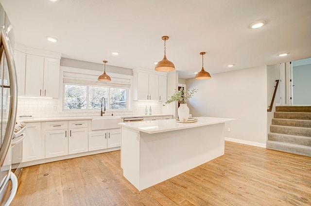 kitchen with sink, white cabinetry, decorative light fixtures, stainless steel fridge, and a kitchen island