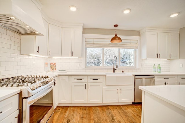 kitchen with sink, appliances with stainless steel finishes, hanging light fixtures, white cabinets, and custom exhaust hood