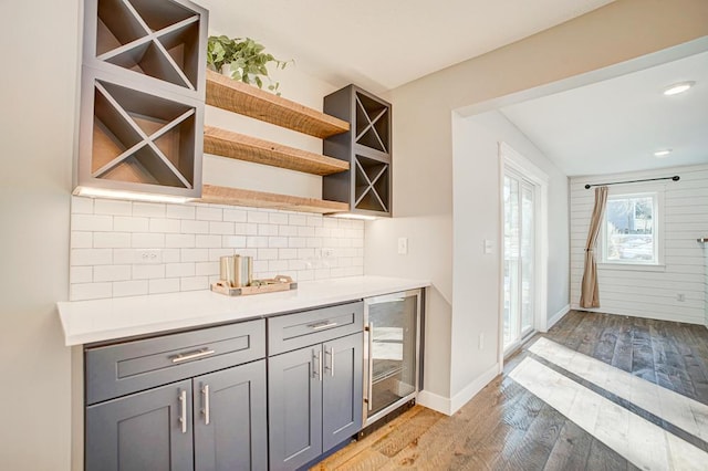 bar with decorative backsplash, beverage cooler, gray cabinets, and light hardwood / wood-style flooring