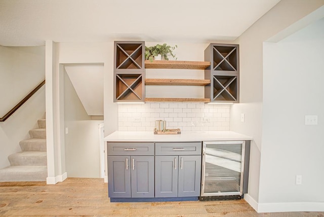 bar with tasteful backsplash, gray cabinetry, beverage cooler, and light hardwood / wood-style floors