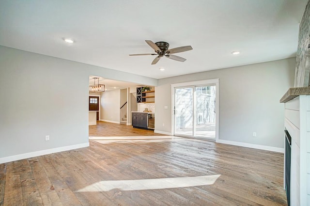 unfurnished living room with ceiling fan with notable chandelier and light wood-type flooring