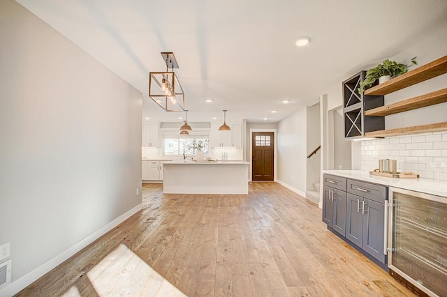 kitchen featuring a kitchen island, tasteful backsplash, white cabinets, hanging light fixtures, and light hardwood / wood-style flooring