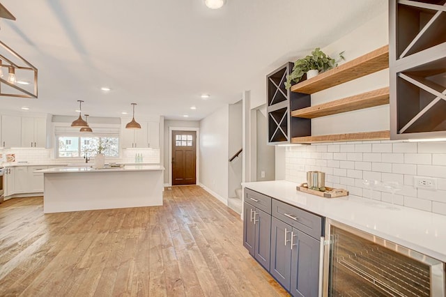 kitchen featuring white cabinetry, tasteful backsplash, decorative light fixtures, beverage cooler, and light wood-type flooring