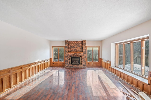 unfurnished living room with wood walls, hardwood / wood-style floors, a brick fireplace, and a textured ceiling