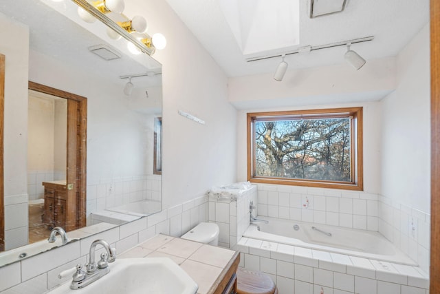 bathroom featuring vanity, tiled bath, and toilet