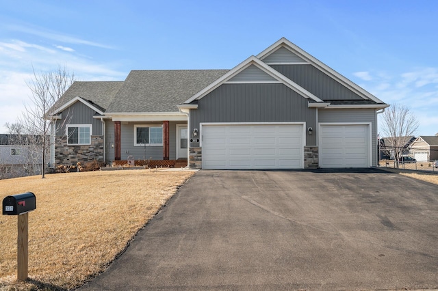 craftsman-style house with a front lawn, aphalt driveway, stone siding, an attached garage, and a shingled roof