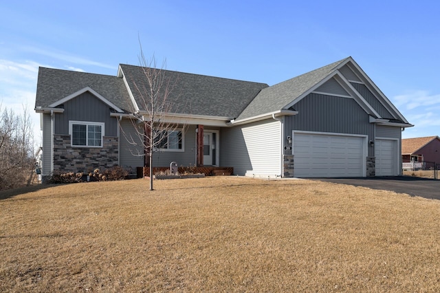 view of front of house featuring a shingled roof, a front lawn, aphalt driveway, stone siding, and an attached garage