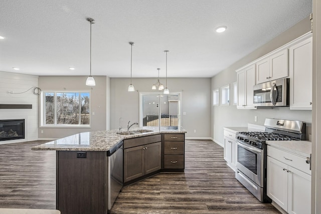 kitchen with dark wood-type flooring, an island with sink, appliances with stainless steel finishes, white cabinetry, and a sink