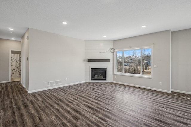 unfurnished living room with dark wood finished floors, visible vents, a fireplace, and baseboards