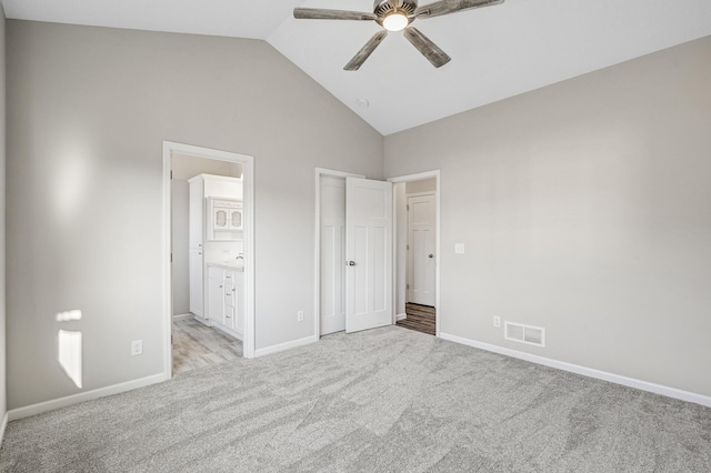 unfurnished bedroom featuring visible vents, ensuite bathroom, baseboards, lofted ceiling, and light colored carpet