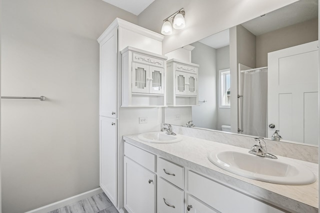 bathroom featuring double vanity, toilet, baseboards, and a sink