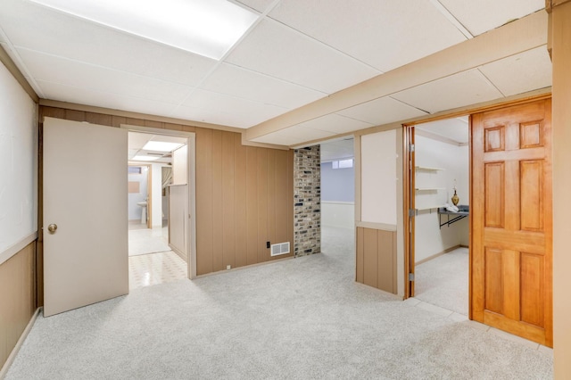 carpeted spare room featuring a drop ceiling and wood walls